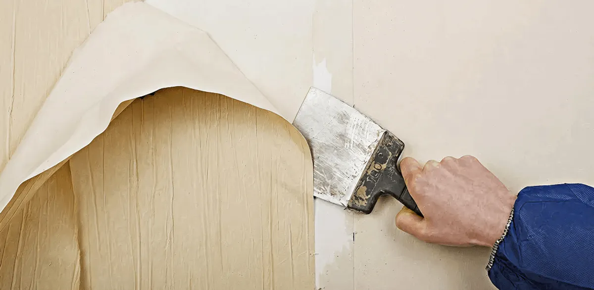 Handyman removing wallpaper with a scraper for wall preparation in Henderson, NV